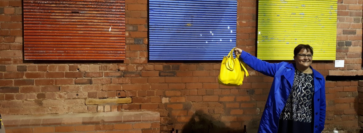 helga henry stands in front of a wall with three panels in red, blue, and yellow, she is smiling as her clothes match the wall